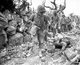 Japan / USA: US Marines pass through a destroyed village where a Japanese soldier lies dead. Battle of Okinawa, May 1945