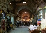 Aleppo's Great Bazaar (in Arabic, <i>suq</i> or <i>souq</i>) as we know it today was rebuilt first by the Egyptian Mamelukes who drove out the Mongols, and then, after 1516, by the Turks who incorporated Aleppo into the Ottoman Empire.<br/><br/>

During the Syrian Civil War, which started in 2011, Aleppo's historic <i>suqs</i> suffered serious damage.<br/><br/>

Aleppo, the second city of Syria and quite possibly the longest continually inhabited settlement in the world, is of venerable age. So old, indeed, that its Arabic name, Halab, is first mentioned in Semitic texts of the third millennium BCE. Situated in the north-west of the country, just a few kilometres from the Turkish frontier, Aleppo is located at the confluence of several great trade routes and, as a city of commerce, has always been rich.